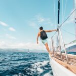 man wearing backpack standing on side of boat during daytime