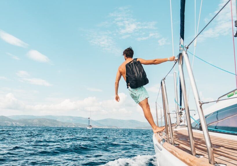 man wearing backpack standing on side of boat during daytime